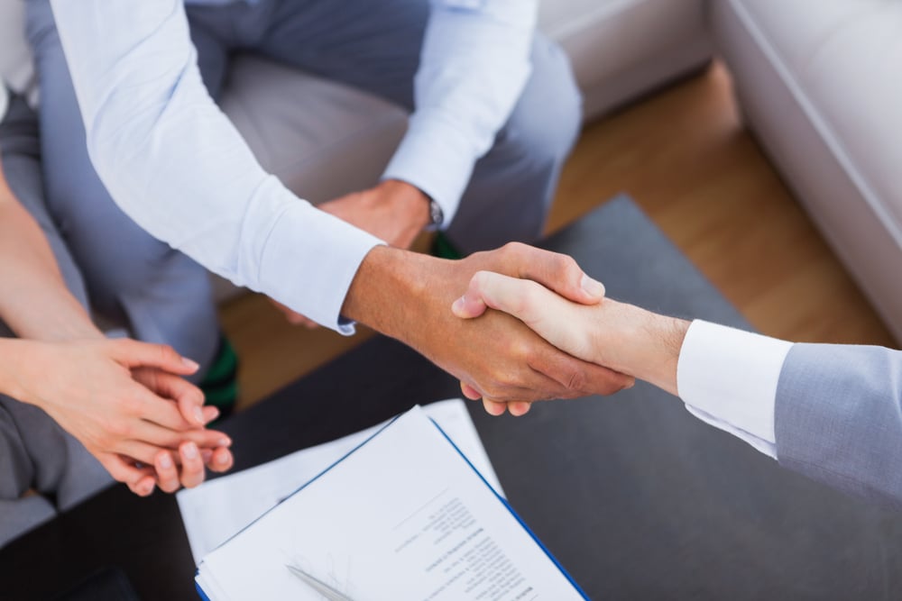 Salesman shaking hands with client with contract on the coffee table-1